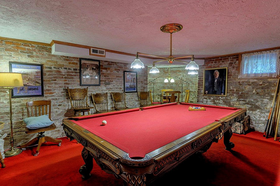 Billiard room with red velvet of the Old Consulate Inn with portrait of Victorian gentleman and other pictures on the wall