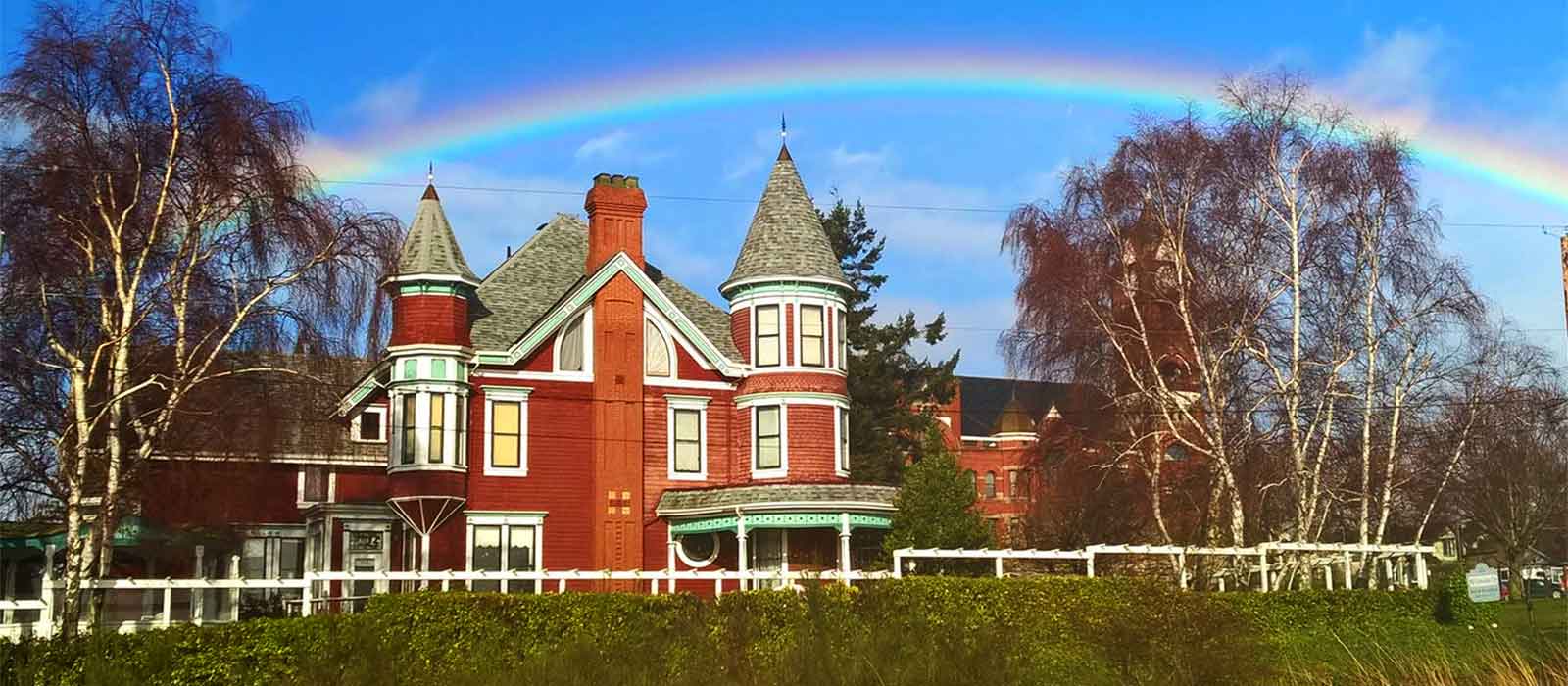 Side view of the Old Consulate Inn beneath a rainbow with the Jefferson County courthouse in the distance